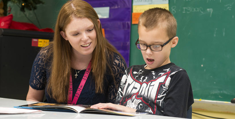 Young male GPA student reading with female teacher 