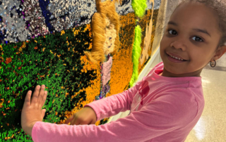 Elementary-aged female GPA student playing with interactive wall art at the school